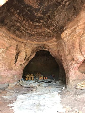 Stacks of items are visible inside a cave with rough, textured walls, and large sheets of material are spread out on the ground.