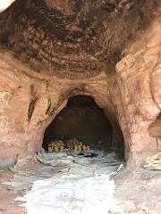 Stacks of items are visible inside a cave with rough, textured walls, and large sheets of material are spread out on the ground.