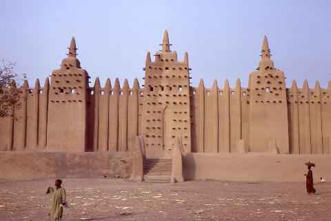 Discover Mali in 7 Days: From the Magic of Timbuktu to the Mud-Brick Marvels of Djenné A grand, earthen mosque dominates the landscape, with children walking in the foreground, creating a scene of everyday life against an ancient backdrop.