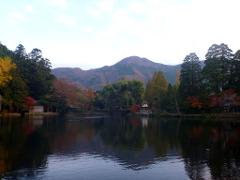A serene lake reflects the surrounding trees and mountains under a soft sky.