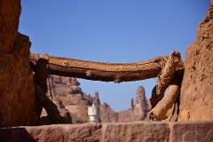 A window view of desert rock formations framed by a rustic wooden structure against a clear blue sky.