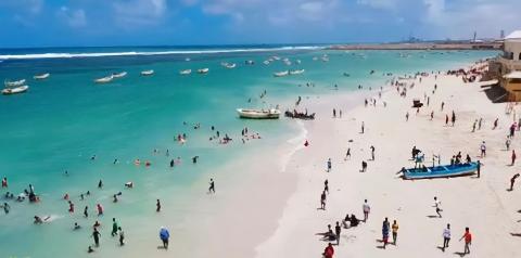 Tur privat de 3 zile în Mogadiscio (istorie, cultură și coastă) This image shows a crowded beach in Mogadishu with people swimming, relaxing, and boats scattered in the turquoise water.