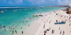 Tur privat de 3 zile în Mogadiscio (istorie, cultură și coastă) This image shows a crowded beach in Mogadishu with people swimming, relaxing, and boats scattered in the turquoise water.