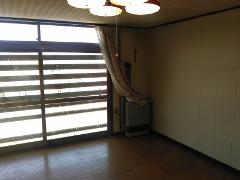 An empty room with a large window, wooden floor, and a portable heater near the window.