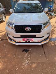 A white Toyota Land Cruiser Prado is parked outdoors, with its license plate reading "TG WZ K-1079 CK" prominently displayed.