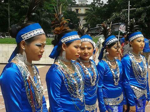 Five women in traditional blue attire, complete with headbands, jewelry, and unique makeup, stand in a row.