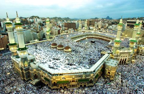 A high-angle view shows the Kaaba and the Masjid al-Haram in Mecca, Saudi Arabia, packed with pilgrims during the Hajj.