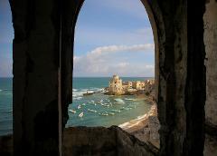 Tur privat de 3 zile în Mogadiscio (istorie, cultură și coastă) An arched window frame reveals a coastal scene with a building, beach, turquoise water dotted with boats, and a blue sky with fluffy clouds.