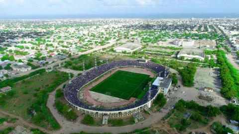 Tur privat de 3 zile în Mogadiscio (istorie, cultură și coastă) An aerial view shows a packed stadium in Mogadishu surrounded by a city with a coastline in the background.