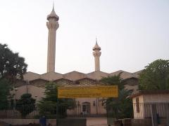 A mosque with two towers is viewed from ground level behind a fence with trees.
