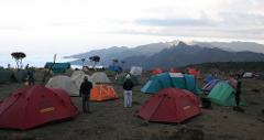 A campsite with numerous colorful tents is set against a backdrop of misty mountains and clouds.