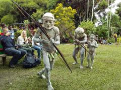 A captivating image displays Papua New Guinean performers with painted bodies and masks, holding spears, engaging in a cultural performance for onlookers on a grassy field.