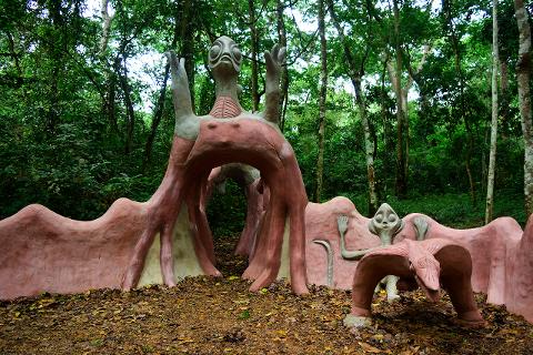 Surreal alien-themed sculptures stand in a lush forest, creating an otherworldly and whimsical atmosphere.