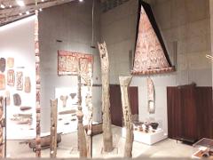 An indoor view of an art museum with totem poles, a wooden canopy, and other cultural artifacts.