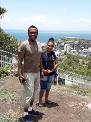 A man and a woman are posing for a photo in Port Moresby, with the city and ocean as the backdrop.