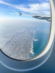 Aerial view of Dubai, including the Palm Jumeirah and Burj Al Arab, seen through an airplane window with a blue sky above.