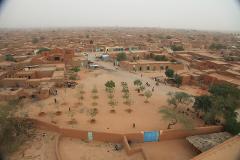 Aerial view of Agadez, Niger, showcasing its traditional mud-brick architecture, a central square with young trees, and a sense of community life.