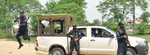 A squad of armed Pakistani police officers poses near a white truck amidst a green outdoor setting.