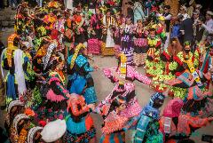 A vibrant scene of Kalash women in colorful traditional dresses dancing in a circle during a cultural event, surrounded by onlookers.