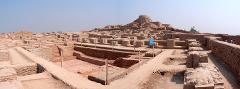 Panoramic view of the archaeological site of Mohenjo-daro, with its ancient brick structures and a central stupa on a raised mound.