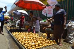 A bustling outdoor market scene with a large display of potatoes, vendors, and customers under umbrellas.
