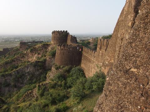 An elevated view of Rohtas Fort, featuring its formidable walls, watchtowers, and lush greenery on the terrain.