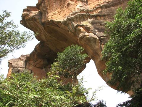 5 Day Bamako – Siby – Ségou – San Cultural Circuit A natural rock archway is framed by lush green trees and the weathered, orange-brown rock formations.