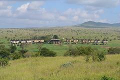 A scenic shot of a hotel with round, stilt-supported huts in a grassy field, set against a backdrop of rolling hills and a cloudy sky.