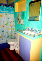 A colorful bathroom in Bocas del Toro features a butterfly shower curtain, turquoise walls, and a custom-tiled countertop vanity with a blue cabinet.