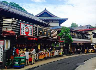 En gadescene i Japan med traditionelle butikker med tempellignende arkitektur under en delvist overskyet himmel.