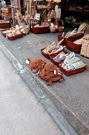 En udstilling på gaden af vævede varer, herunder måtter og kurve, arrangeret i brune beholdere og direkte på fortovet uden for en butik.