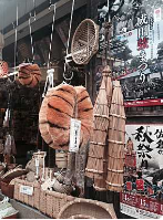 En butiksudstilling fremviser traditionelt japansk håndværk som vævede kurve, bambusparaplyer og tigerstribede dekorationer, sammen med en plakat, der reklamerer for en festival.