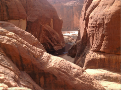 A scenic view of a river flowing through a desert canyon in Chad, with a herd of camels gathered near the water source.