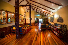 The image showcases a spacious resort lobby with wooden floors and exposed beam ceilings, furnished with comfortable seating areas, carved posts, and decorative displays.