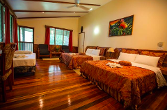 This is an interior shot of a Tawali resort room in Milne Bay/Alotau with wooden floors, beds with patterned covers, chairs by a window, and a painting on the wall.