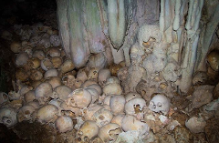 This chilling image depicts a cave filled with numerous human skulls, situated near stalactites, creating a macabre and eerie scene.