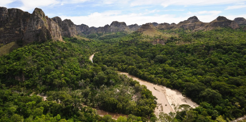 A panoramic shot of a lush green valley with a winding river, surrounded by towering rock formations under a partly cloudy sky.