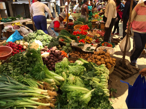A vibrant vegetable market scene, packed with diverse produce, bustling with vendors and shoppers.