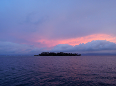 A picturesque view of a tropical island in the middle of the ocean under a captivating twilight sky with vibrant pink and purple hues.
