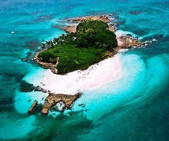 An aerial view of a tropical island with lush greenery and a white sand beach surrounded by turquoise waters.