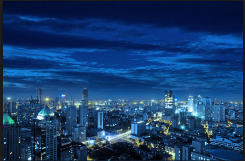 An aerial view of a city at night under a cloudy, dark blue sky.