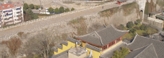 An aerial view of traditional Chinese architecture with yellow walls and tiled roofs, situated near a stone city wall.