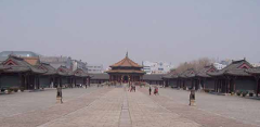 A wide-angle shot of an ancient Chinese courtyard with traditional buildings surrounding a large open space, under an overcast sky.