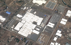 Aerial view of an extensive industrial complex with numerous large, white-roofed buildings and expansive parking areas, likely a manufacturing or distribution center.