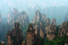 A scenic view of tall, rocky pillars rising from a green, forested valley under a hazy sky.