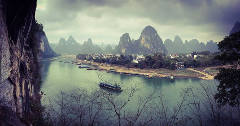 A scenic view of the Li River winding through karst mountains and a village in China on a cloudy day.