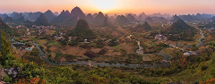 Panoramic landscape of Guilin, China at sunset, featuring karst mountains, a winding river, and agricultural fields.