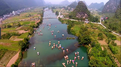 Aerial view of Li River, China, with bamboo rafts carrying tourists under parasols, amidst karst mountains and lush greenery.