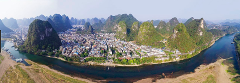 Panoramic view of a town nestled amidst unique karst mountains, bisected by a river with sandy banks.