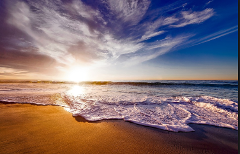 A serene beach scene featuring a bright sunrise, with waves gently washing over the golden sand under a sky filled with soft clouds.